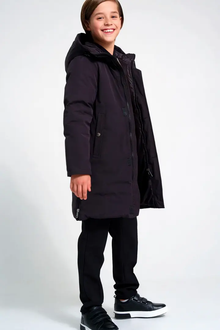 A smiling boy in a dark winter parka turns to show the back and the hood.